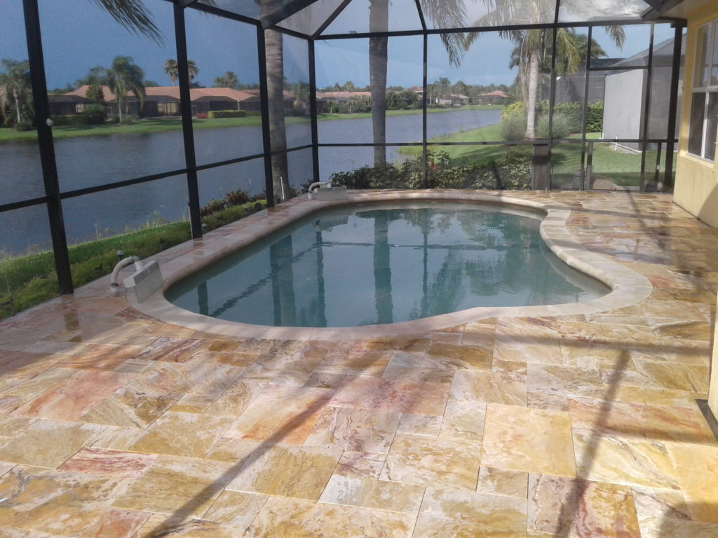 Pool deck with travertine pavers with a cream color and a pool enclosure 